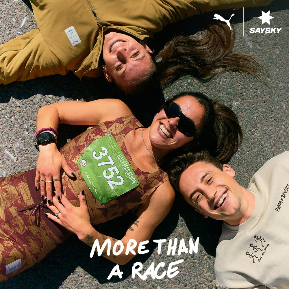 Original campaign still: three runners lying on asphalt laughing after a race, English tagline reading 'More than a race'